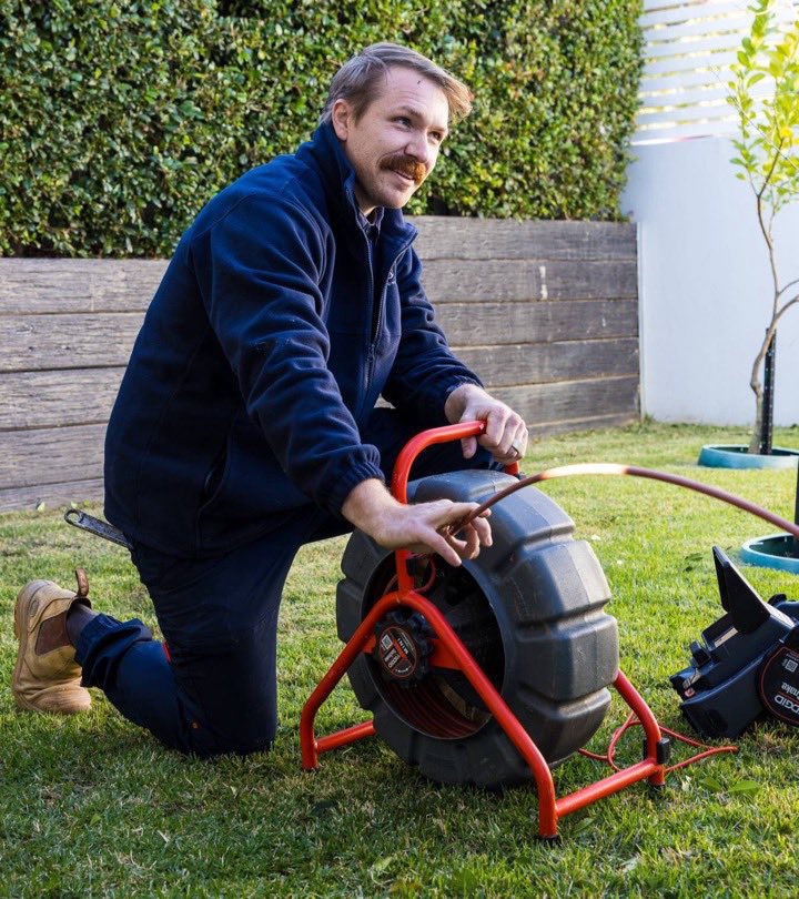 S&J plumber kneeling on a lawn with a drain cleaning machine