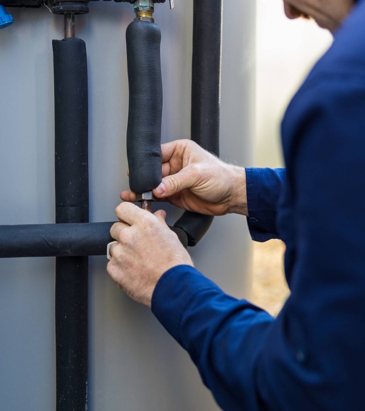 Hands adjusting a valve on wall-mounted hot water pipework